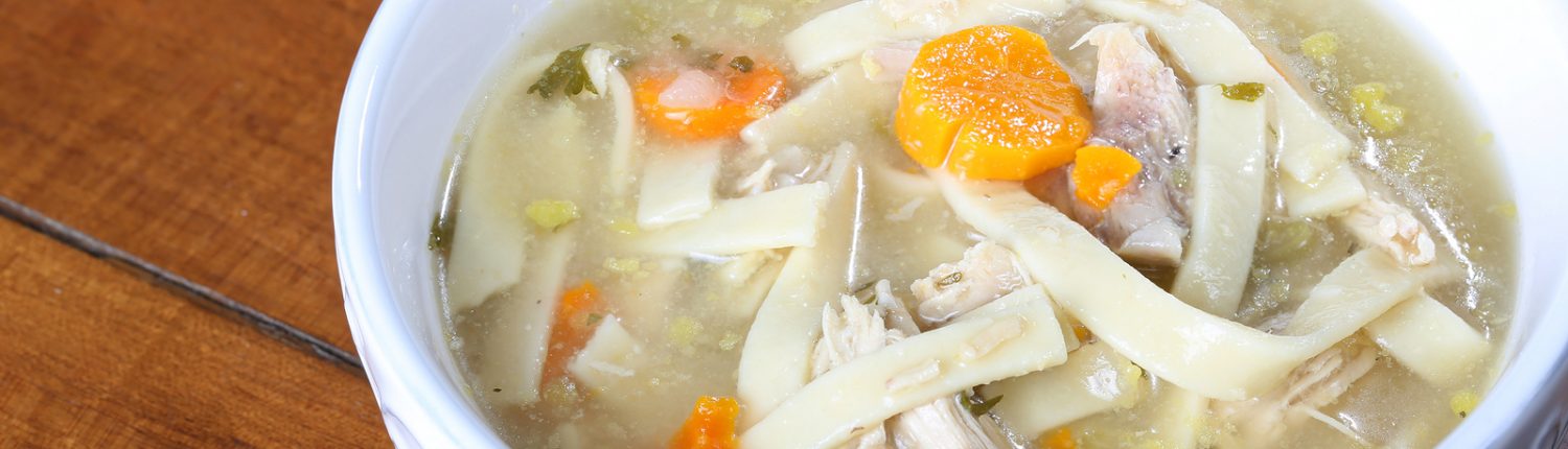 chicken noodle soup in a cream colored bowl ready to eat with large noodles